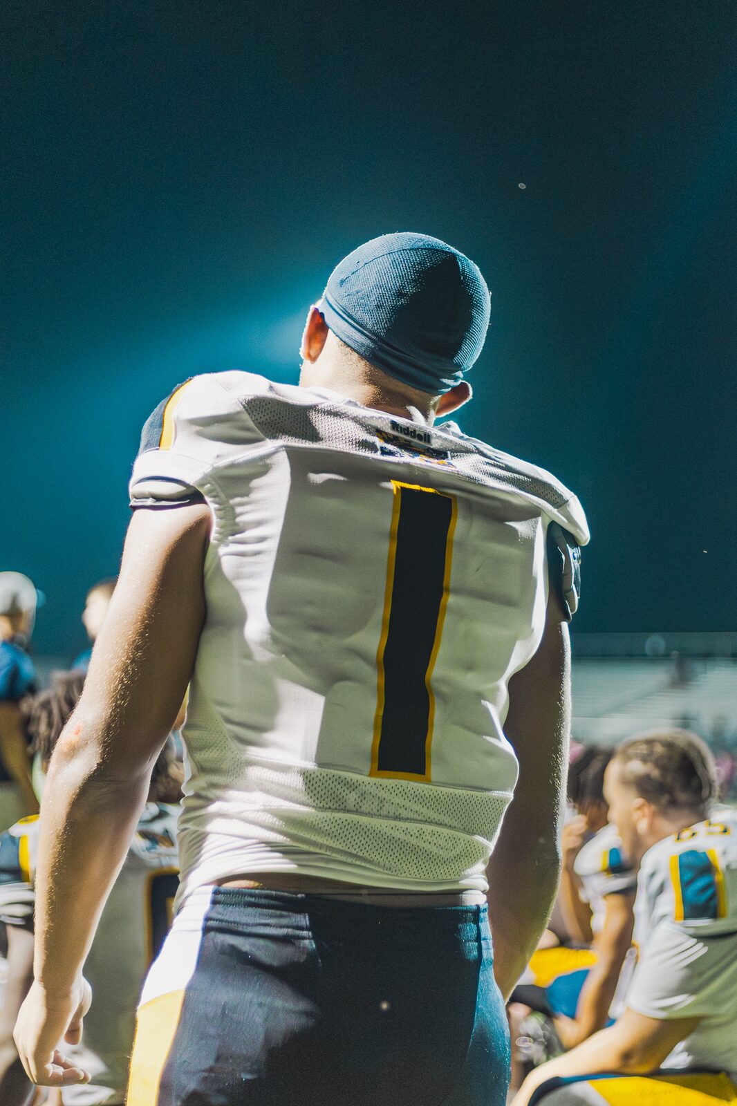 Player number 1 seen from behind on the sideline lit by cool stadium light
