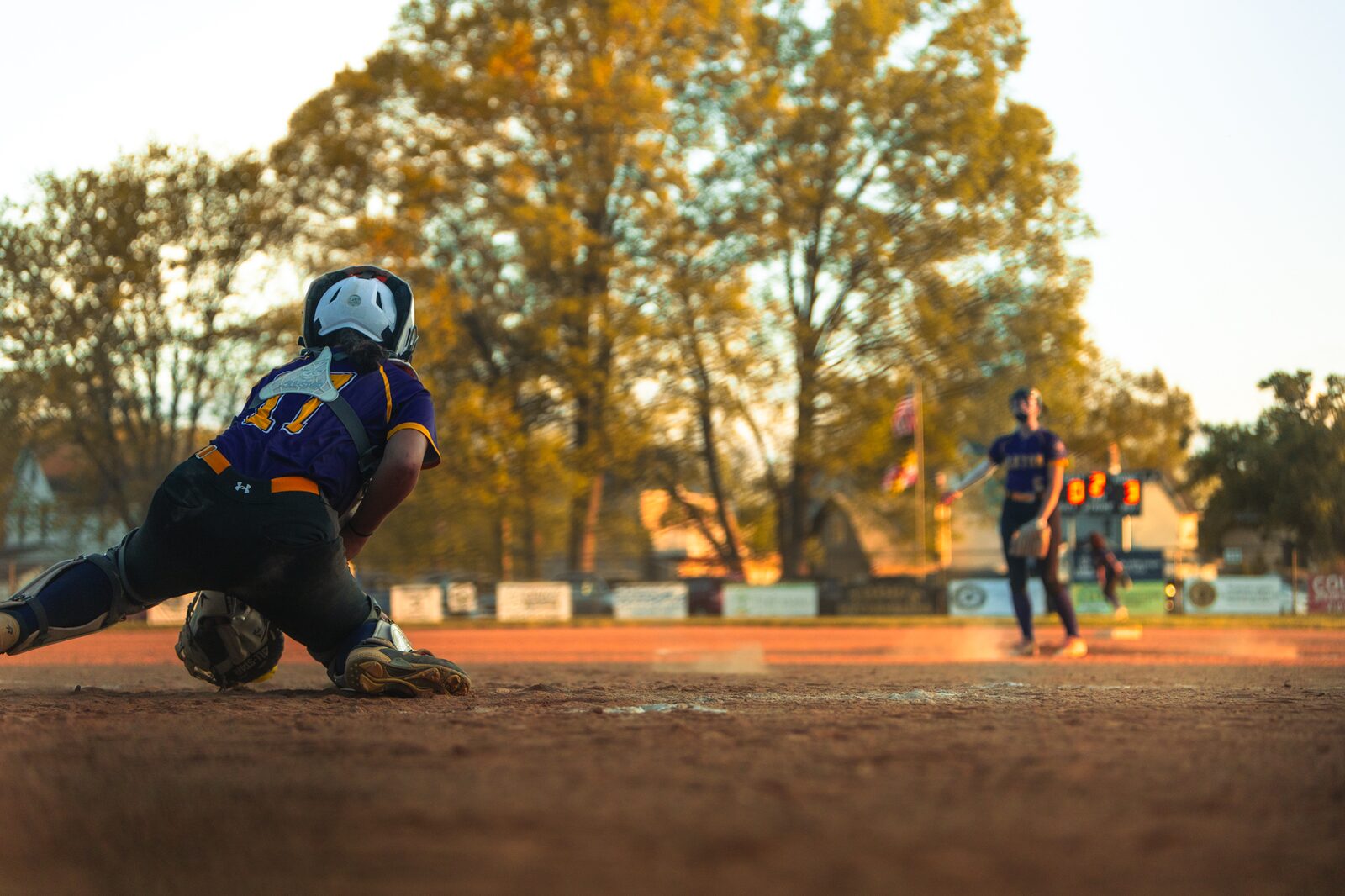 Low angle view of a softball catcher braced at home plate as the pitcher delivers
