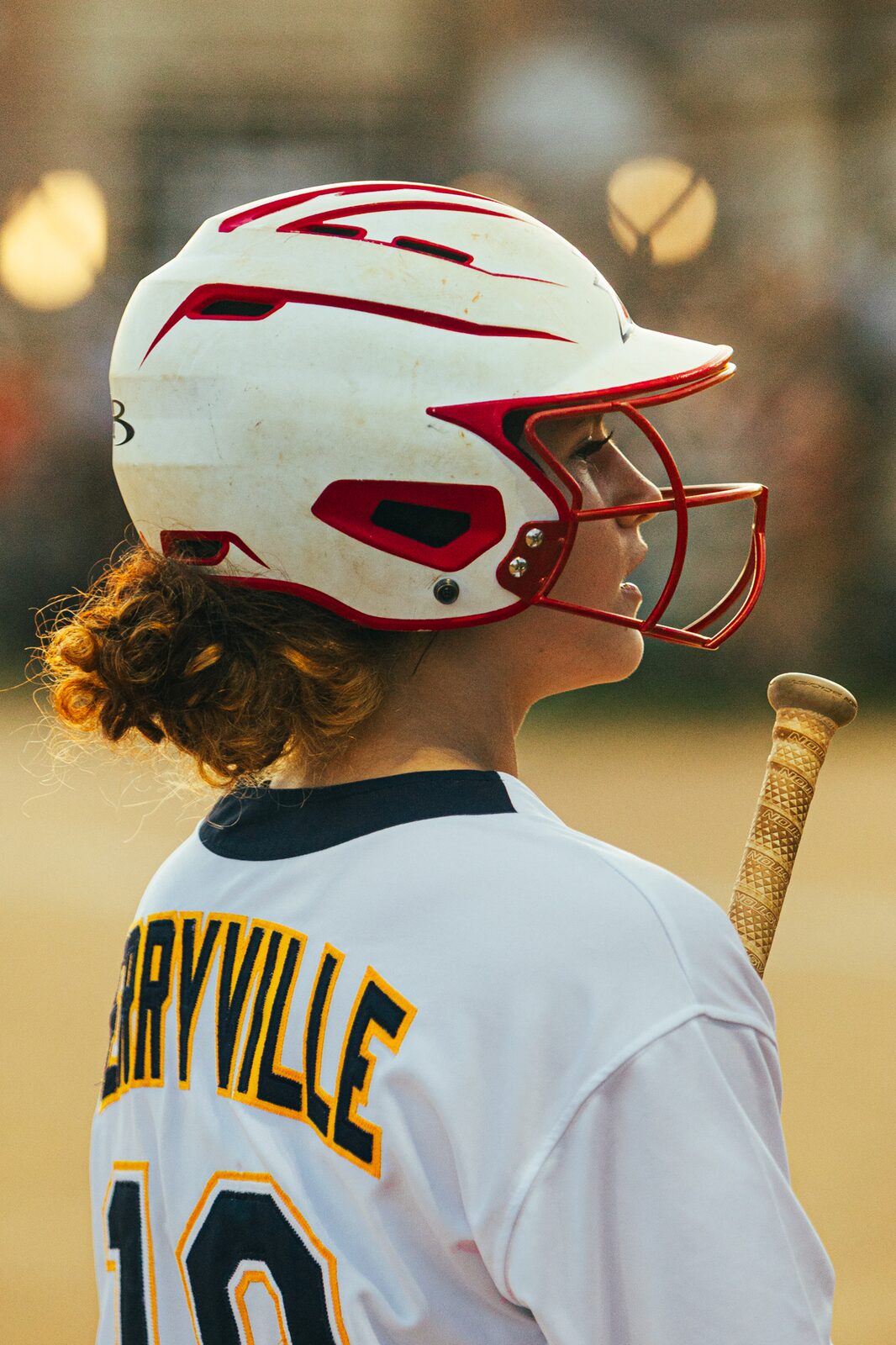 Close portrait of a softball player in a batting helmet resting her bat on her shoulder