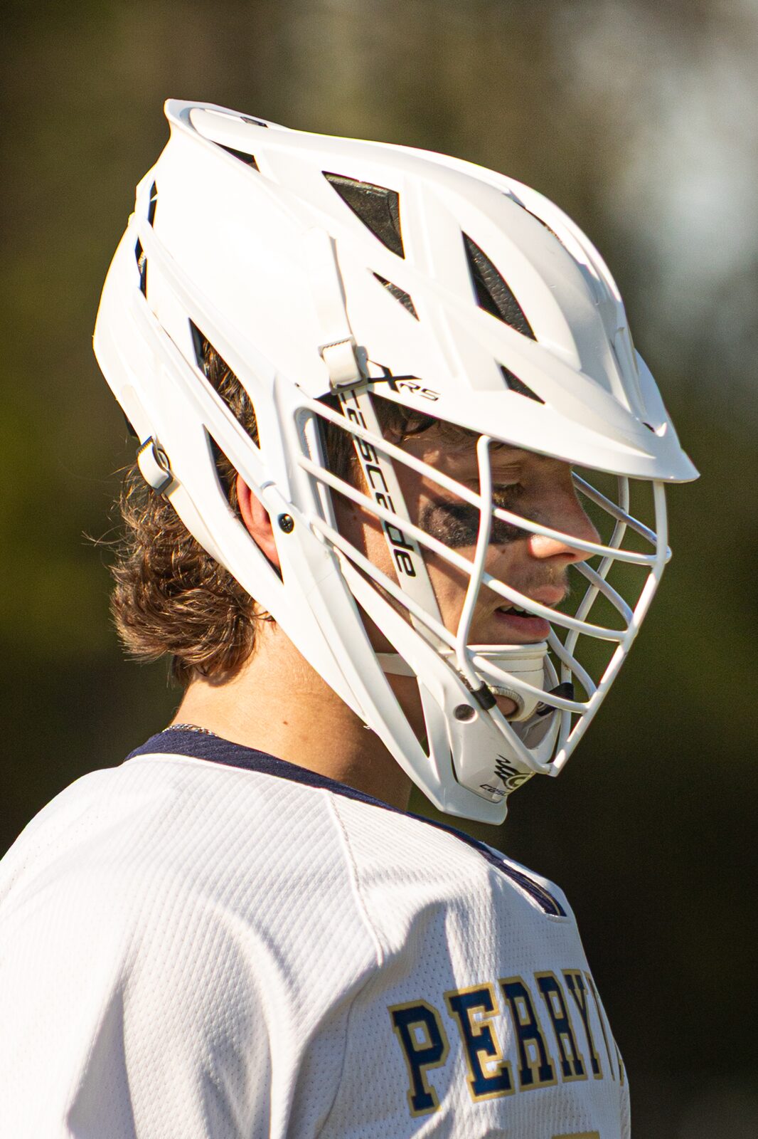 Profile portrait of a lacrosse player in a white helmet against a soft green background
