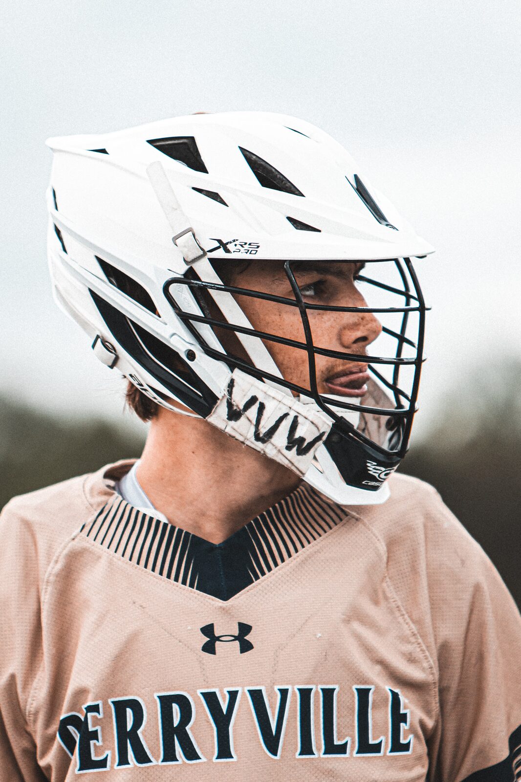 Profile portrait of a lacrosse player in a white helmet looking down the field