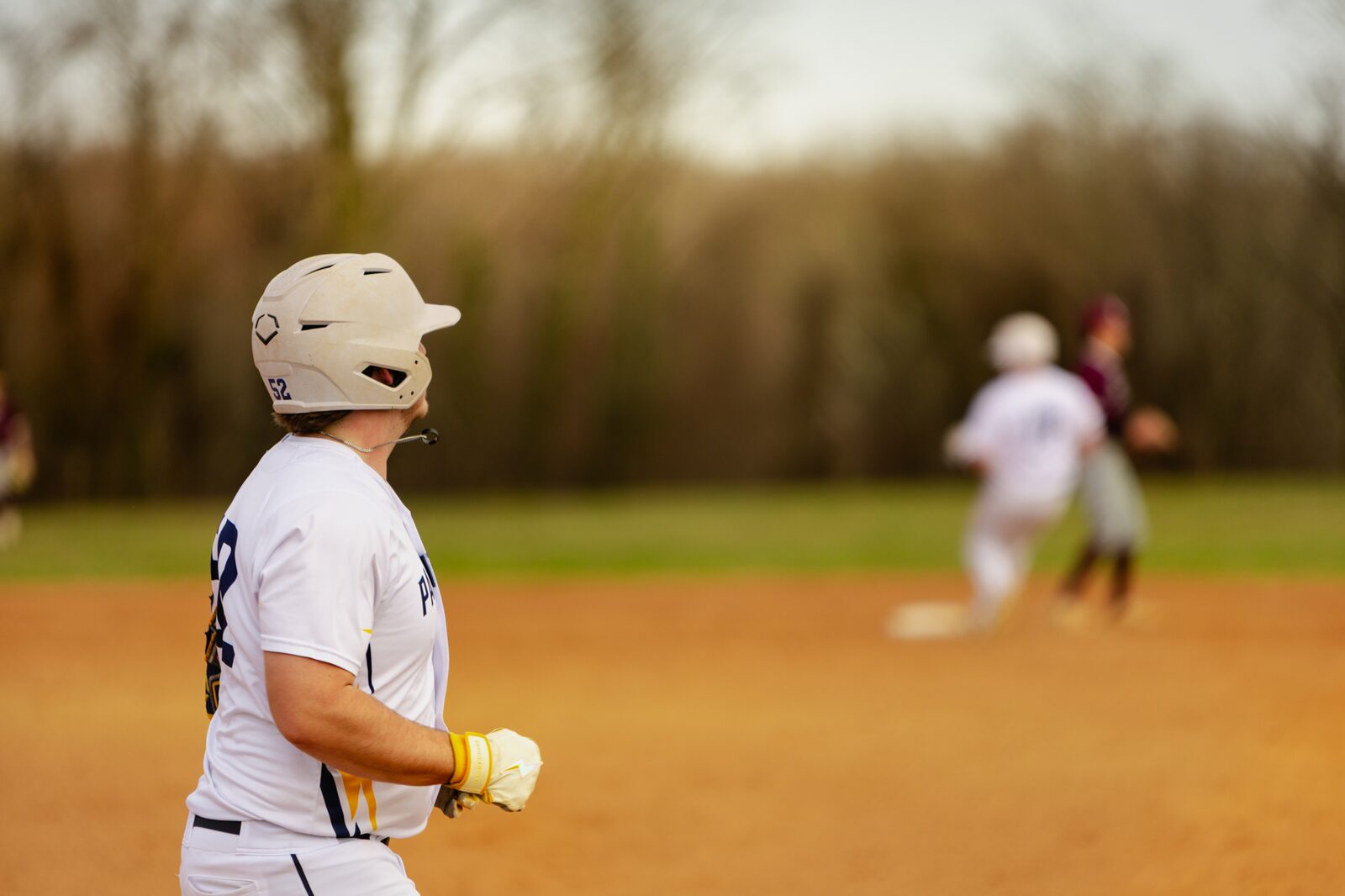 Base runner in a helmet watching the play develop in soft golden light