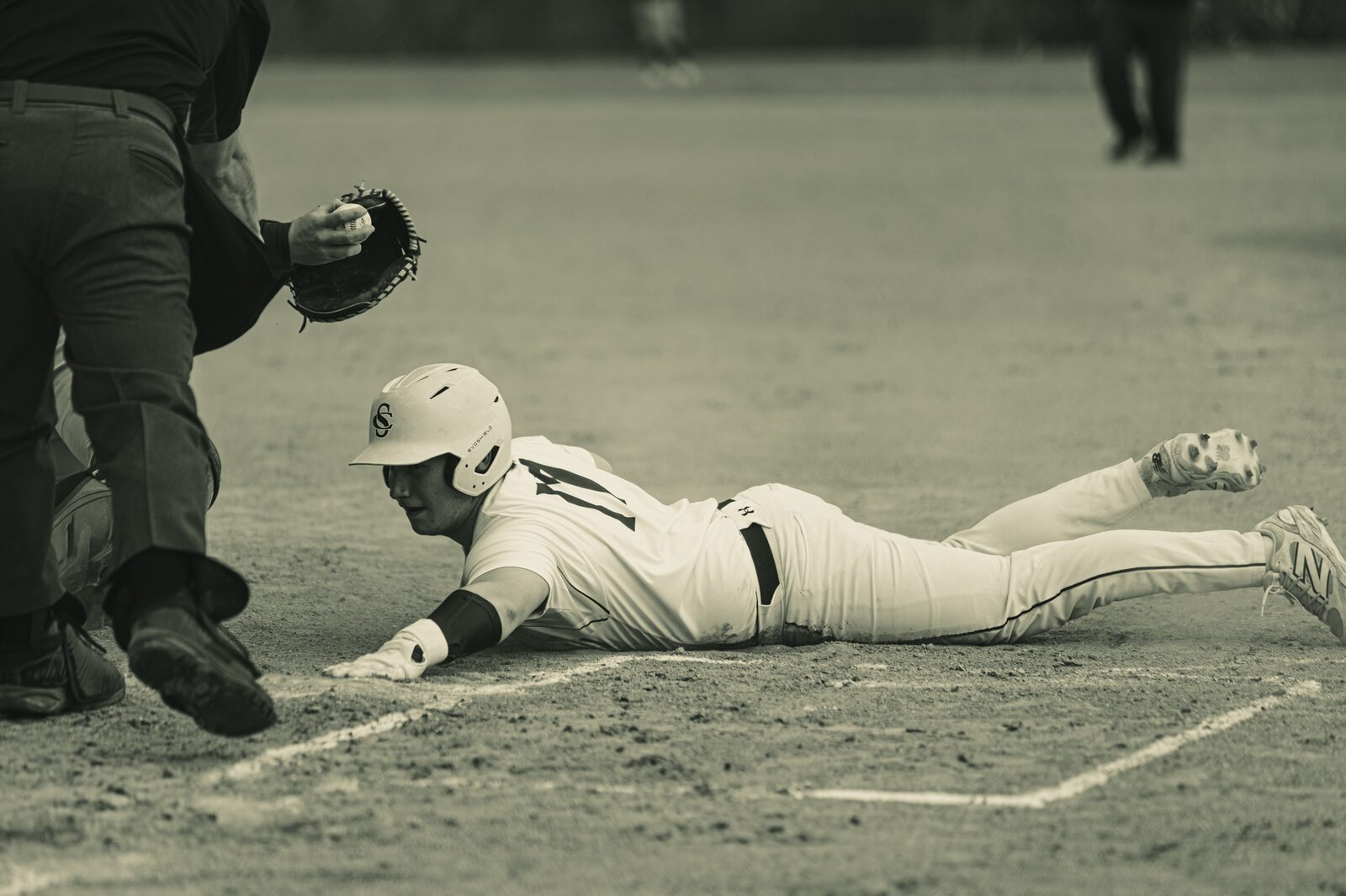 Sepia toned photo of a base runner diving headfirst into the bag as the fielder reaches with his glove