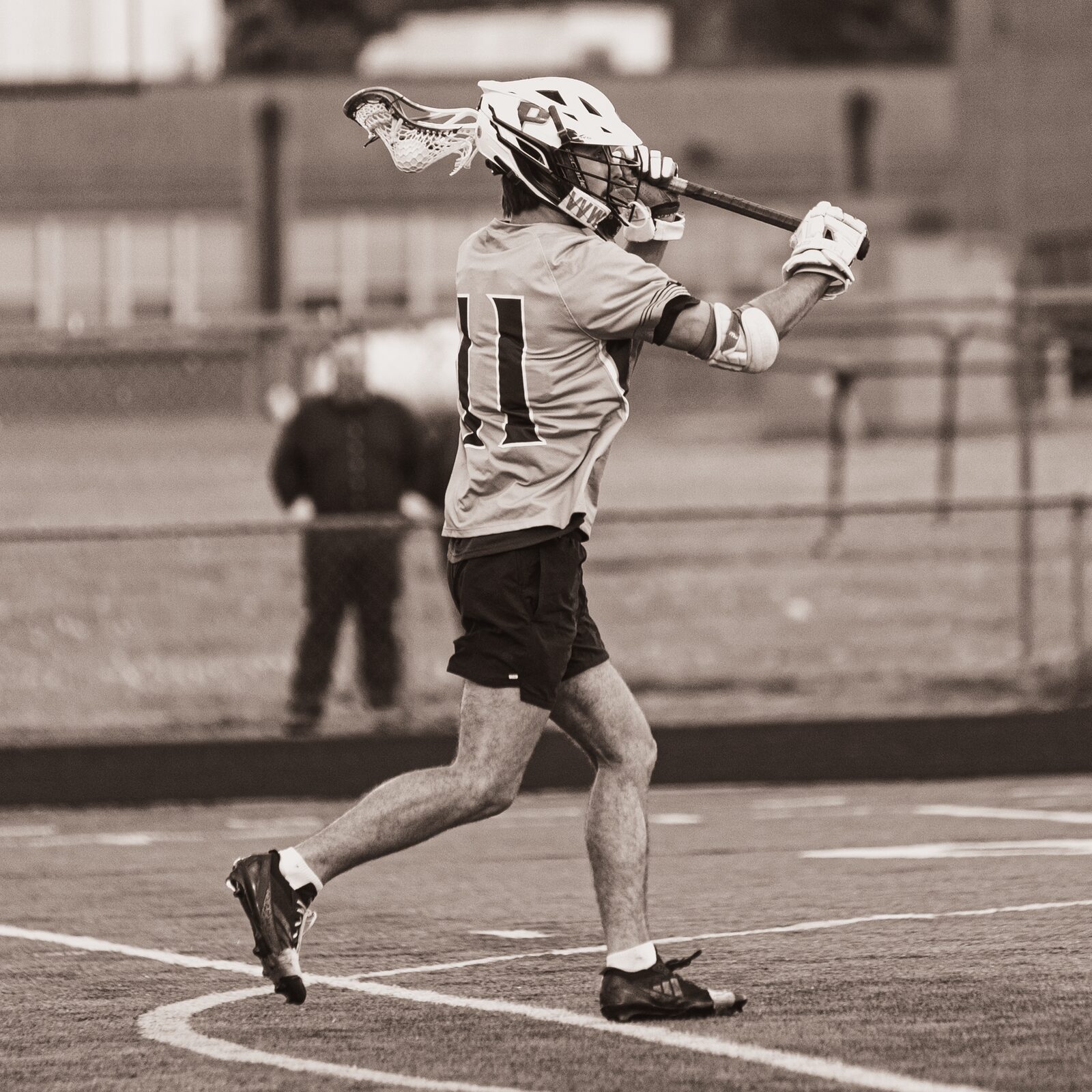 Warm toned photo of a lacrosse player shooting with his stick fully extended
