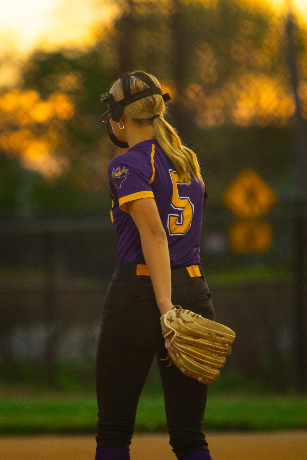 Softball player standing with her glove at her side in golden evening light