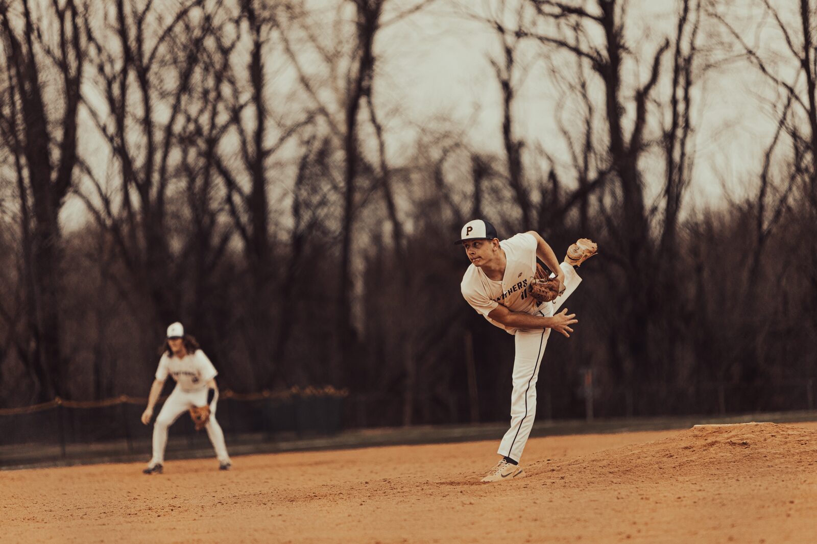 Warm toned wide view of a pitcher following through with an infielder set behind him