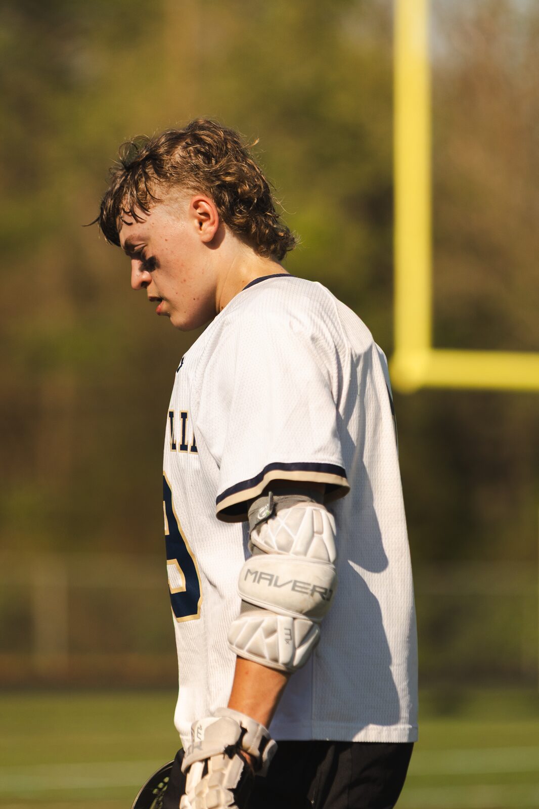 Lacrosse player looking down in front of a yellow goalpost during a day game