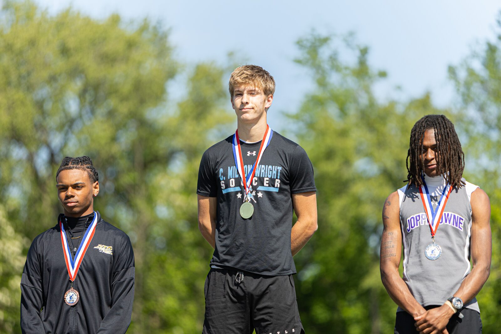 Three athletes standing on the medal podium wearing their medals after an event
