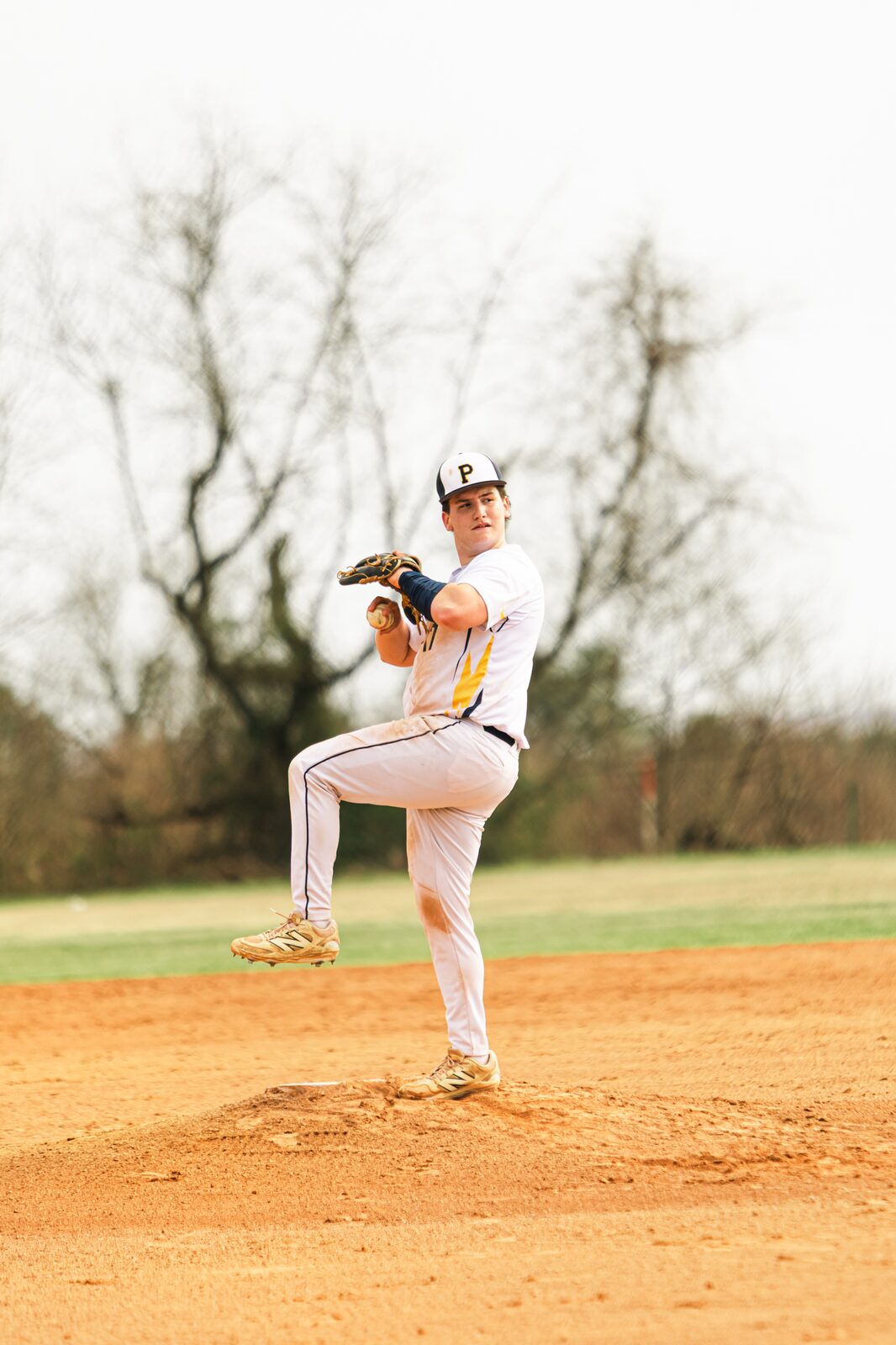 Pitcher at the top of his windup with his front leg raised on the mound