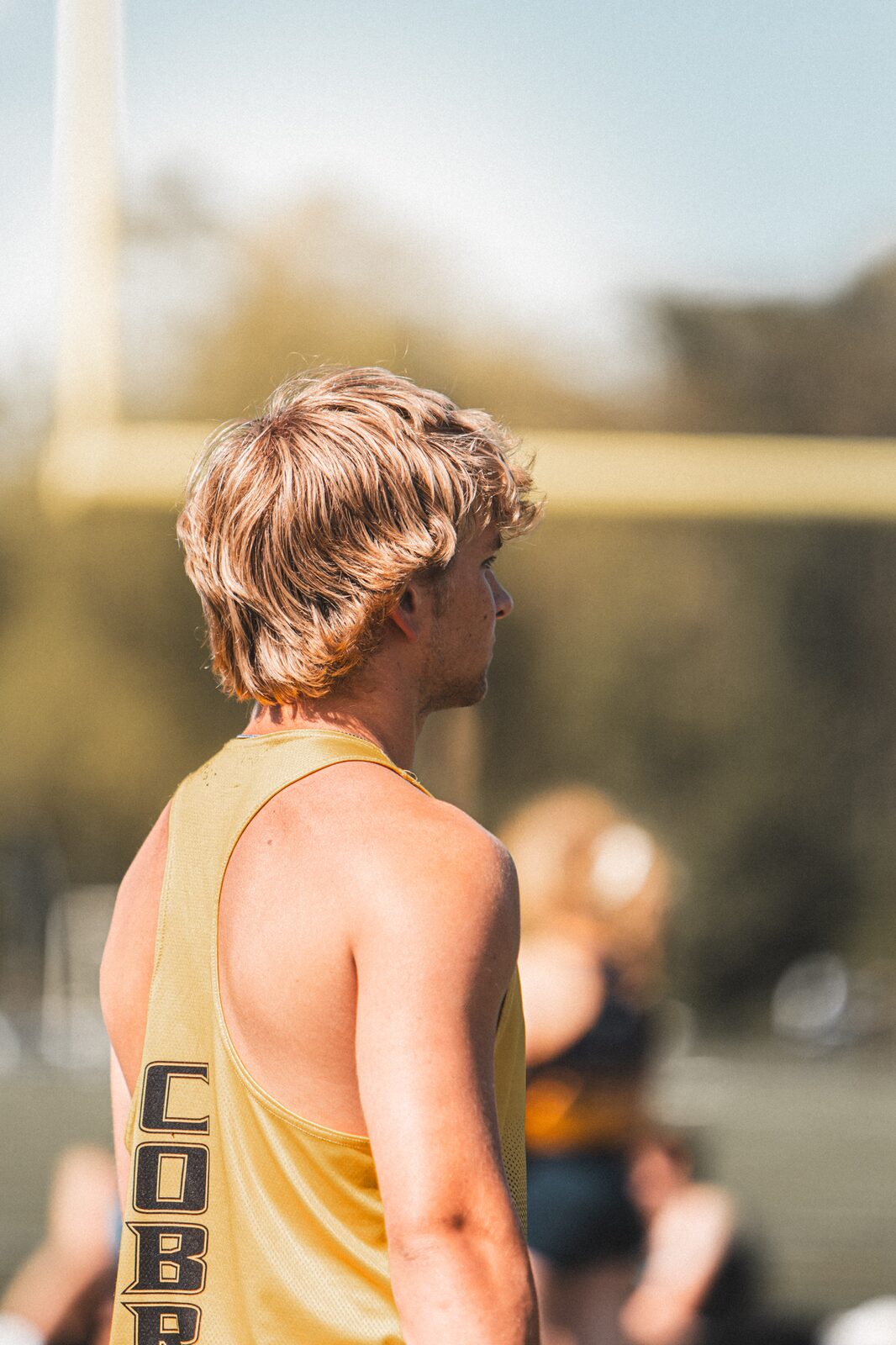 Athlete in a gold singlet seen from behind looking out toward the track