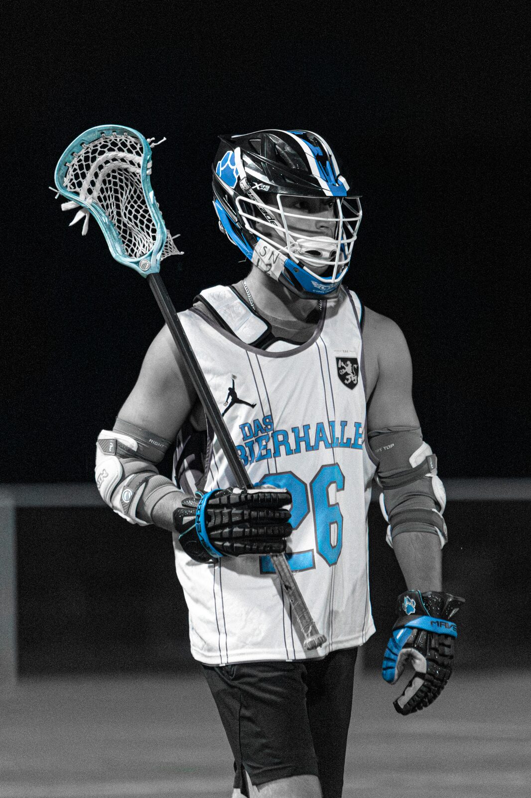 Lacrosse player standing against a black night background with his stick over his shoulder