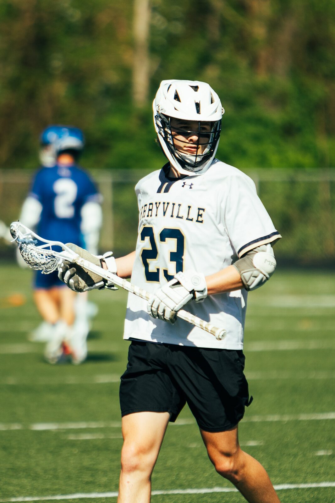 Lacrosse player number 23 running up the field with his stick out in front of him