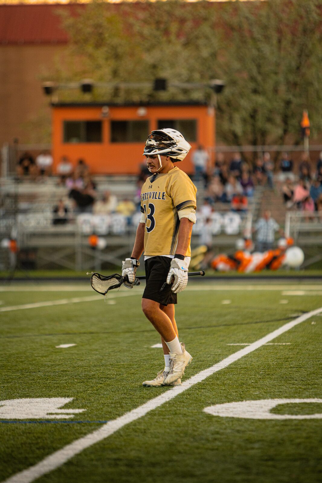 Lacrosse player walking up the field in evening light with a full crowd in the stands behind him