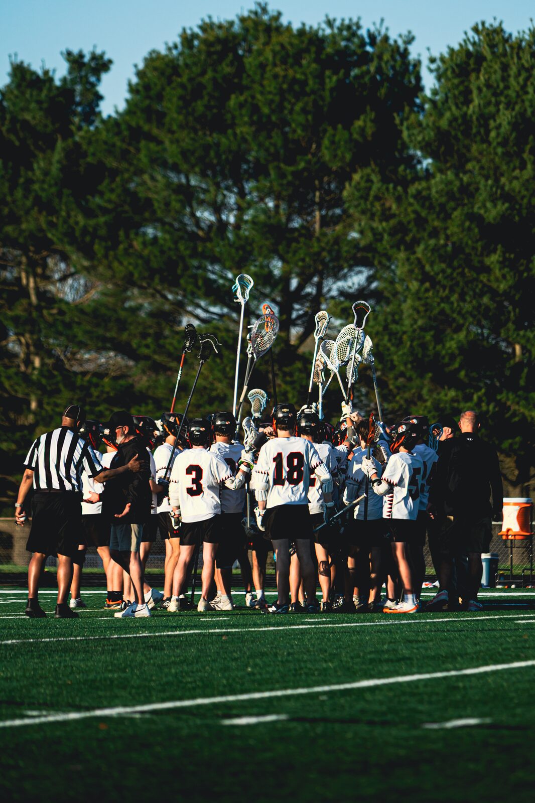 Lacrosse team huddled together on the field in golden evening light