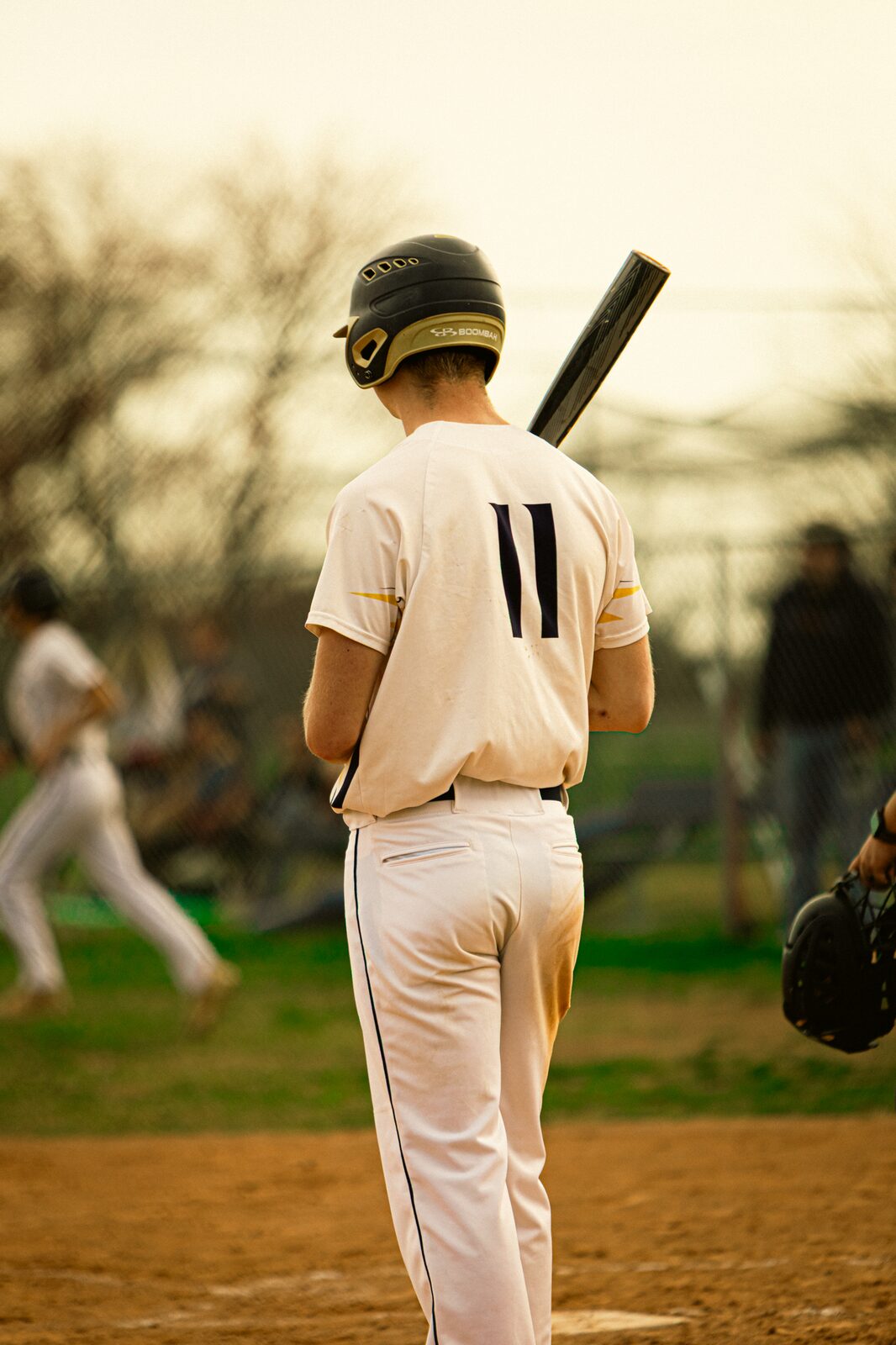 Batter waiting on deck in warm evening light with his back to the camera