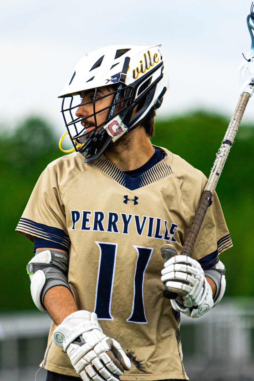 Lacrosse player number 11 holding his stick and looking off camera in daylight