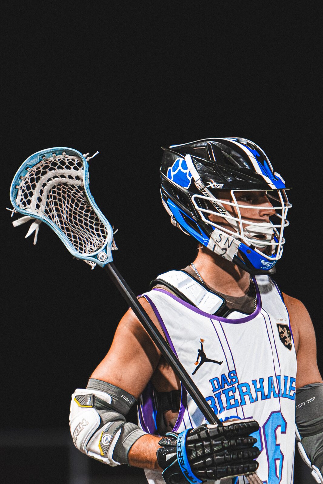 Lacrosse player standing against a black night background holding his stick upright under the lights