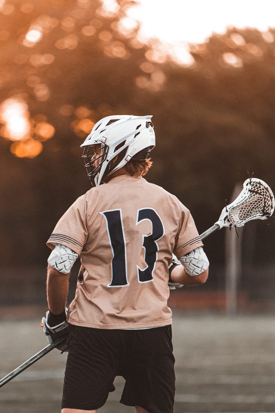 Lacrosse player number 13 standing on the field in warm sunset light
