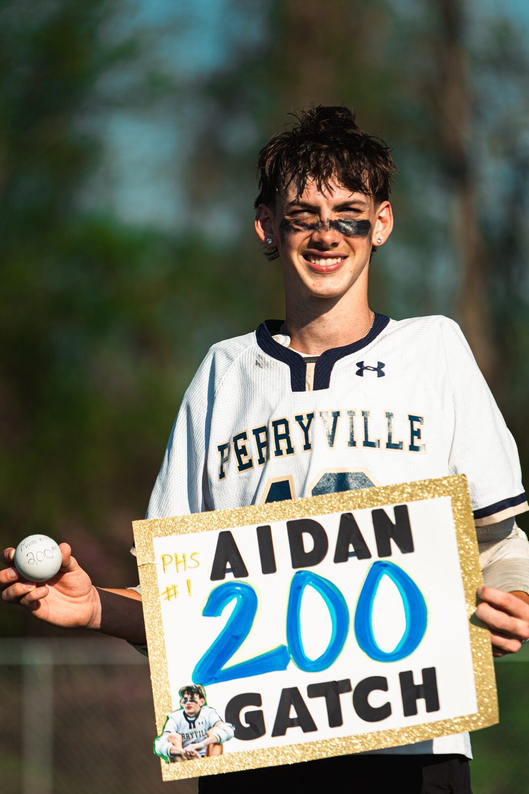 Smiling lacrosse player holding a handmade sign celebrating his two hundredth career goal