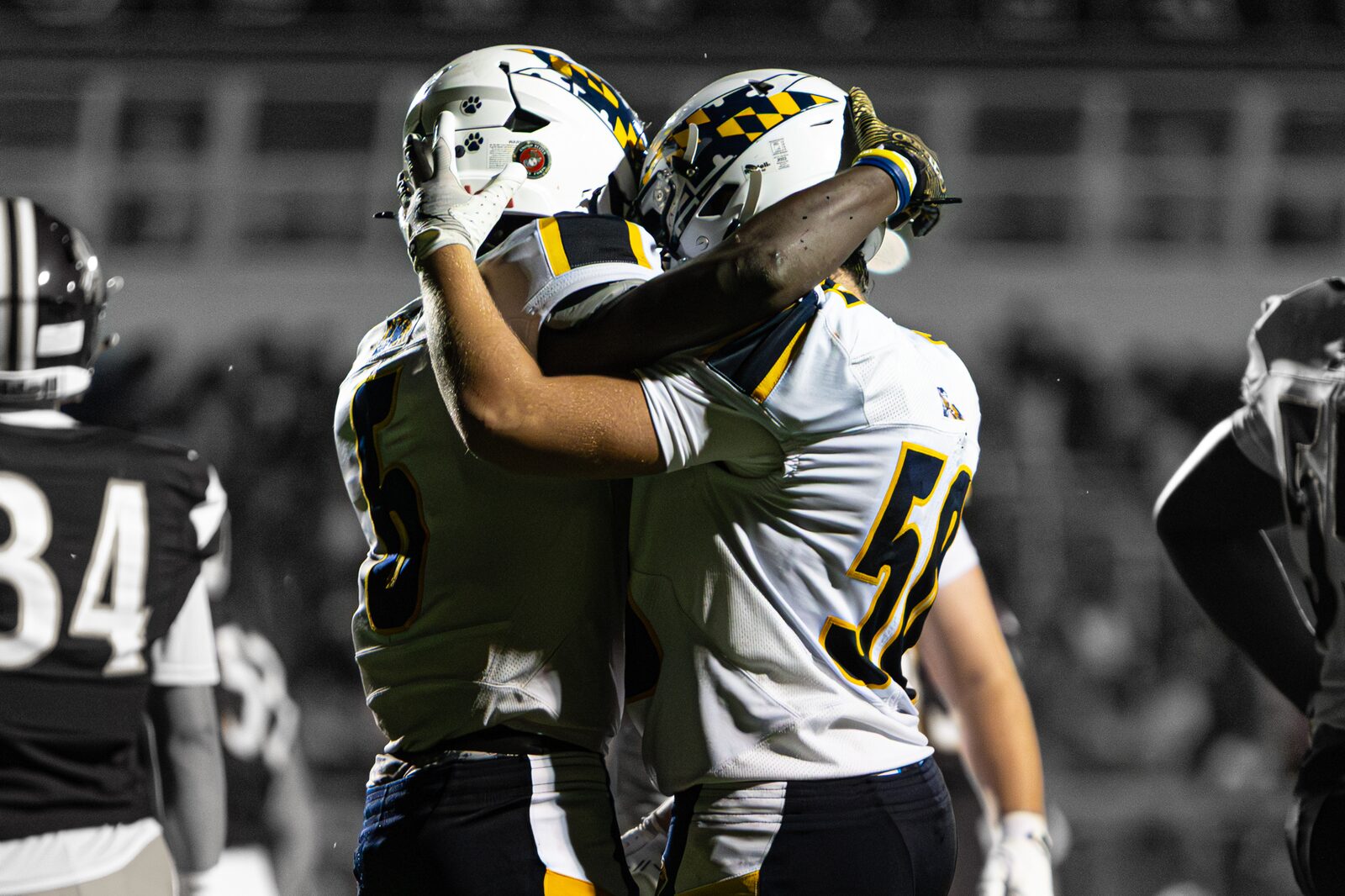 Two teammates embracing helmet to helmet to celebrate a play