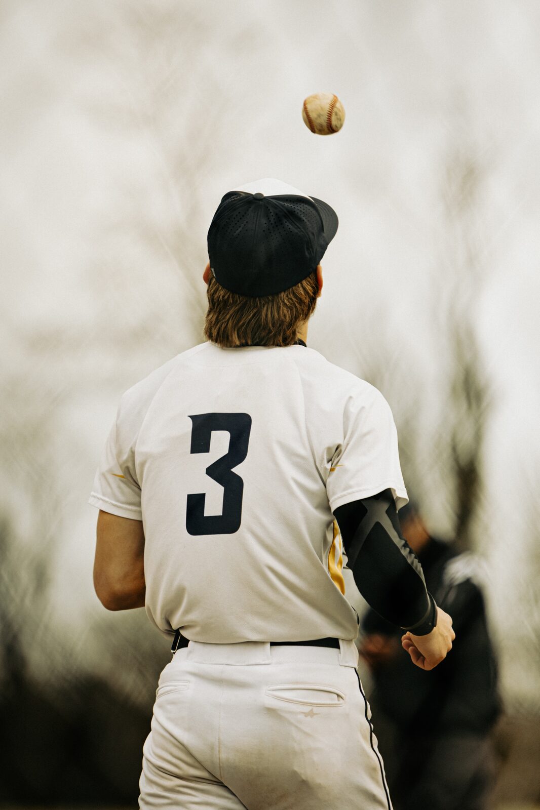 Player seen from behind tossing a baseball up above his head between innings