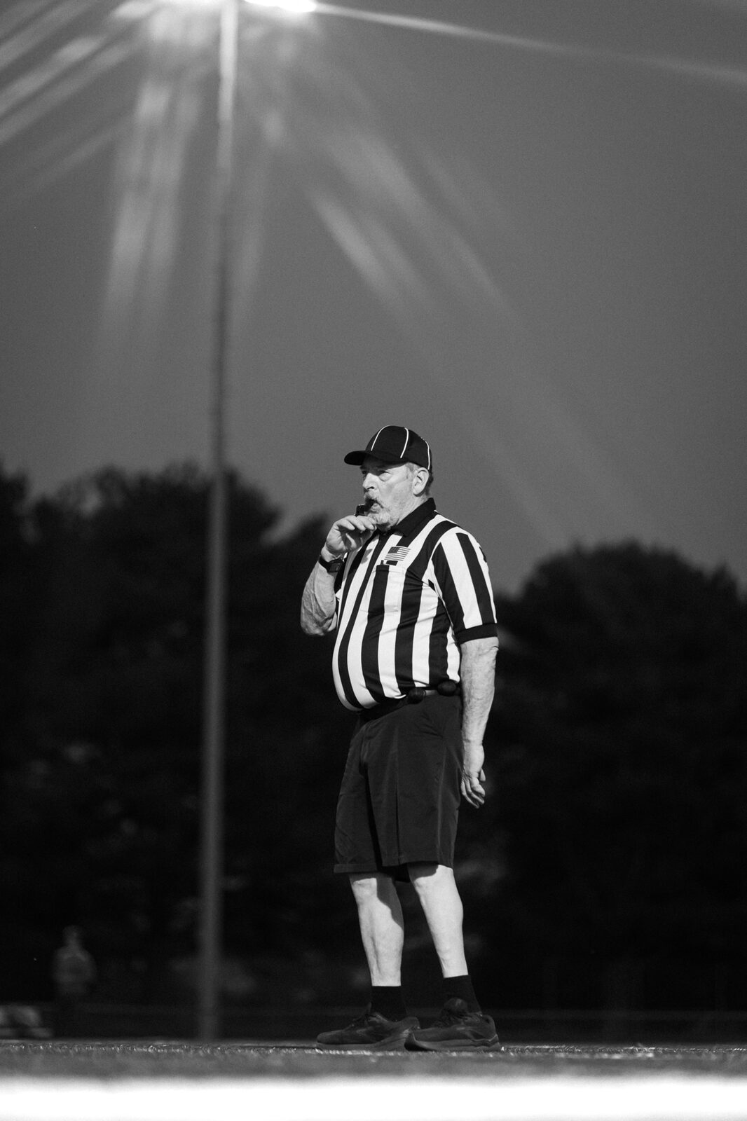 Black and white photo of a game official standing on the field with the sun flaring behind him