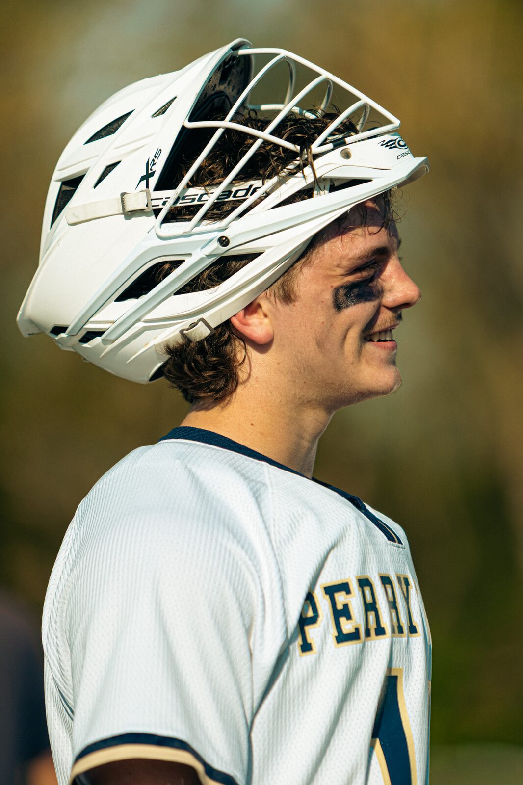 Lacrosse player in a white helmet smiling as he looks toward the sideline