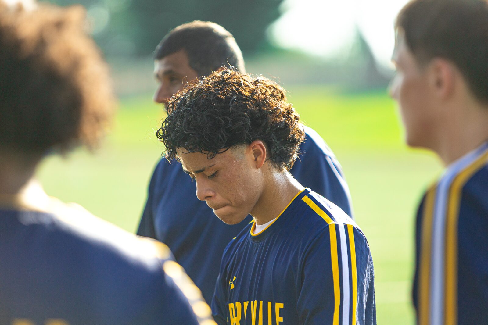 Soccer team standing with heads bowed together in a circle before kickoff
