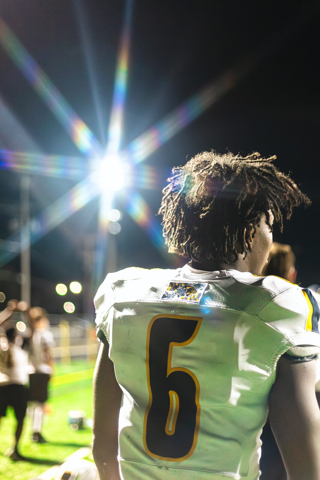 Player number 6 seen from behind on the sideline with a stadium light flaring behind his head