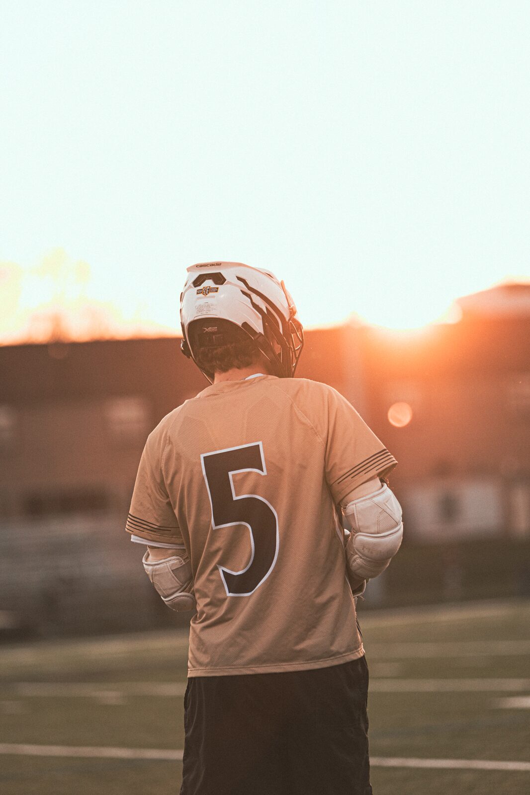 Lacrosse player walking across the field silhouetted by a low orange sun behind the goalpost