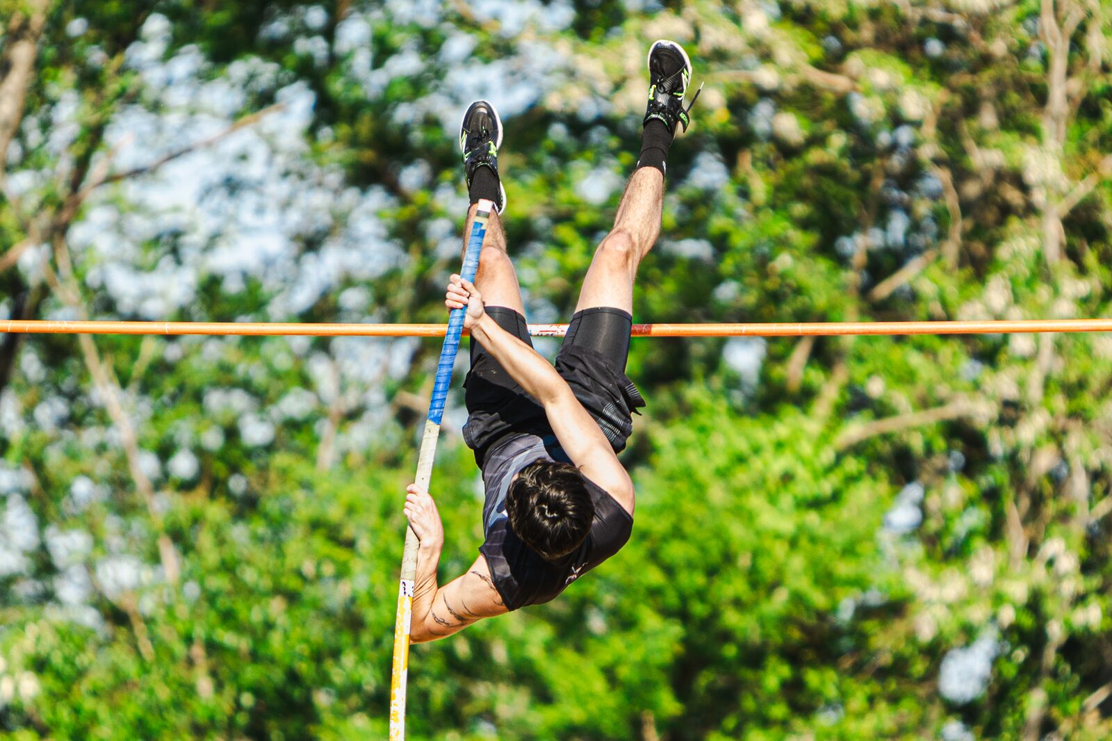Pole vaulter inverted above the bar with the pole bending beneath her